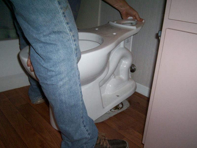 Carefully setting the new toilet onto the wax ring and flange