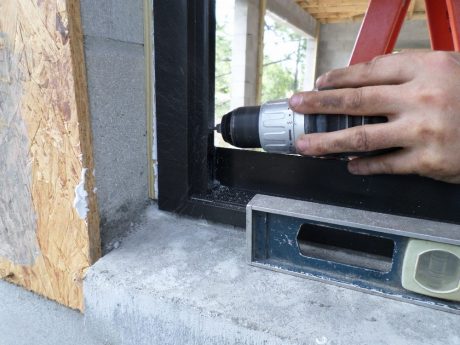 Drilling into the provided hole on the window frame, through the wood window buck and into the solid-poured concrete block cell with a puff of dust
