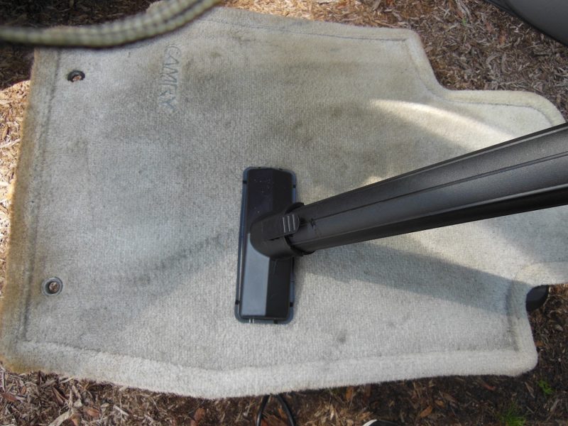Vacuuming a car mat.